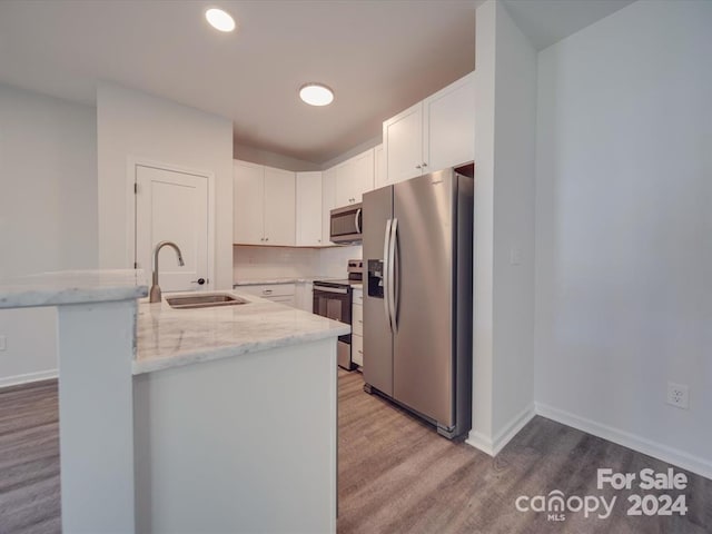 kitchen with sink, hardwood / wood-style flooring, light stone countertops, white cabinetry, and stainless steel appliances