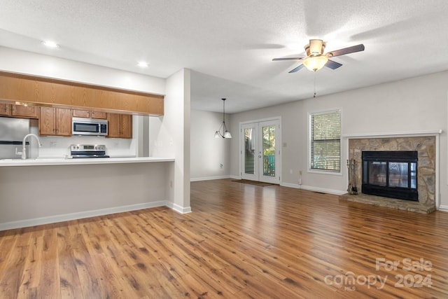 kitchen with kitchen peninsula, hardwood / wood-style floors, stainless steel appliances, and a stone fireplace