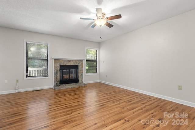 unfurnished living room with a textured ceiling, light hardwood / wood-style floors, a stone fireplace, and ceiling fan