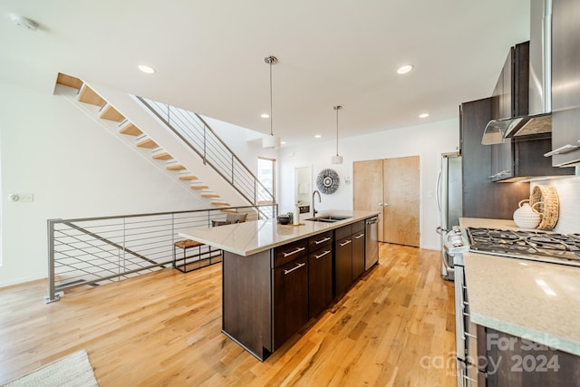 kitchen with appliances with stainless steel finishes, a kitchen island with sink, sink, light hardwood / wood-style floors, and hanging light fixtures