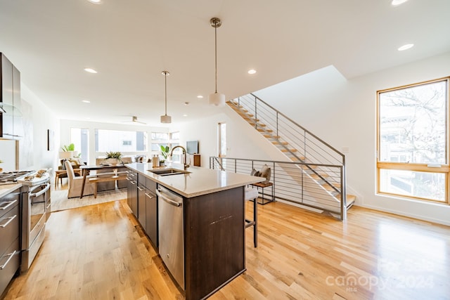 kitchen with pendant lighting, a kitchen island with sink, sink, appliances with stainless steel finishes, and light hardwood / wood-style floors