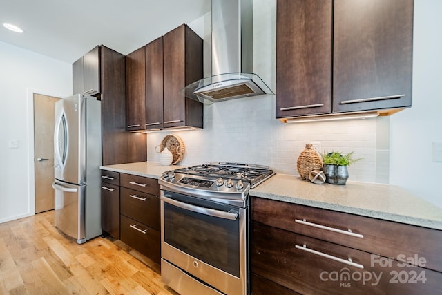 kitchen with light wood-type flooring, light stone counters, wall chimney exhaust hood, dark brown cabinets, and stainless steel appliances