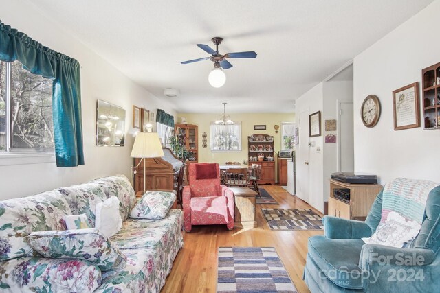 living room featuring ceiling fan with notable chandelier and light hardwood / wood-style flooring