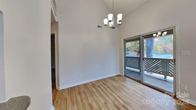 spare room with an inviting chandelier, high vaulted ceiling, and light hardwood / wood-style flooring