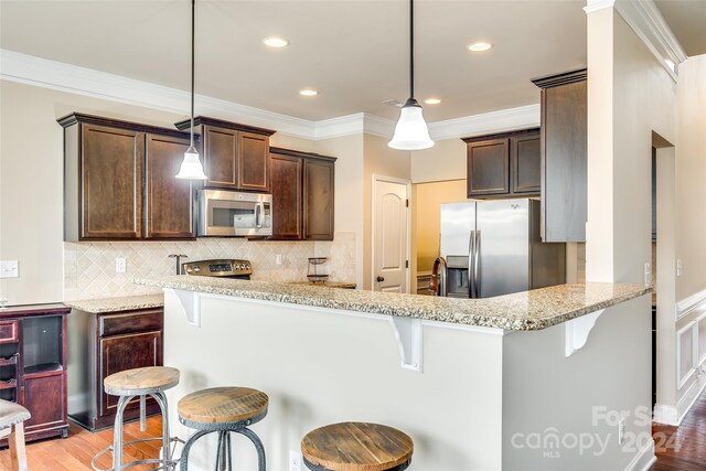 kitchen featuring a breakfast bar, appliances with stainless steel finishes, kitchen peninsula, and pendant lighting