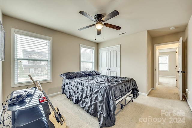 bedroom with a closet, multiple windows, light colored carpet, and ceiling fan