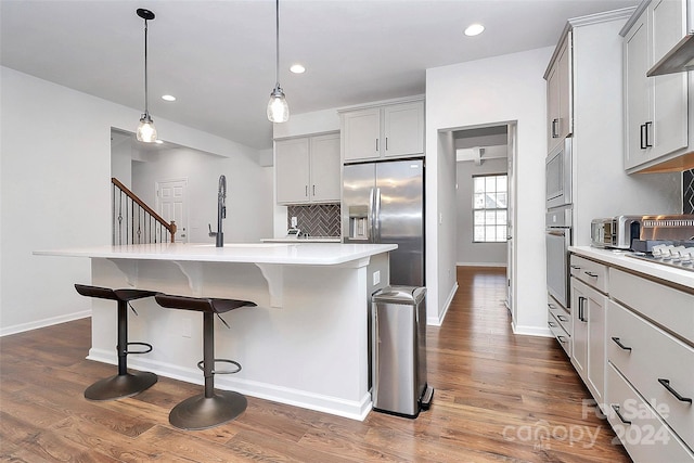 kitchen with decorative light fixtures, stainless steel appliances, a kitchen island with sink, and dark hardwood / wood-style floors