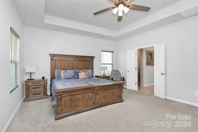 carpeted bedroom featuring a tray ceiling and ceiling fan