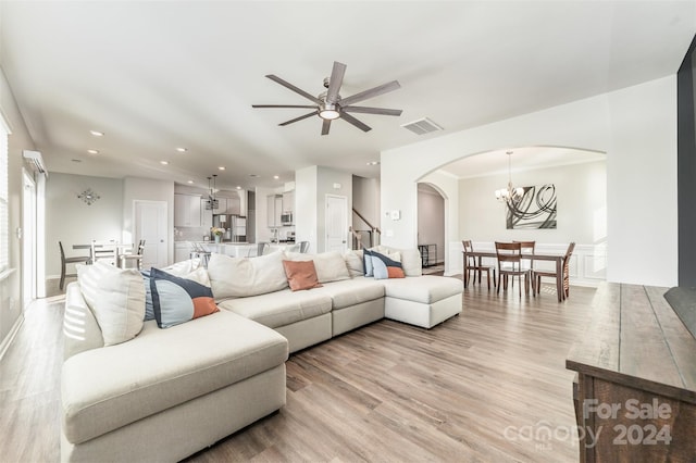 living room with ornamental molding, ceiling fan with notable chandelier, and light wood-type flooring