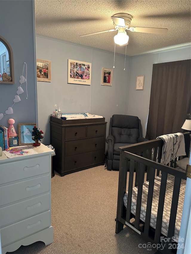 bedroom featuring a crib, ceiling fan, light carpet, and a textured ceiling