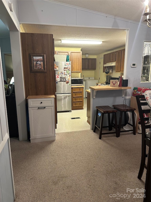 kitchen featuring a kitchen breakfast bar, vaulted ceiling, washer and dryer, a textured ceiling, and stainless steel refrigerator