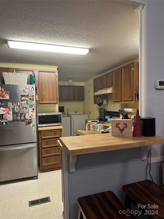 kitchen featuring a kitchen bar, appliances with stainless steel finishes, a textured ceiling, and washing machine and clothes dryer