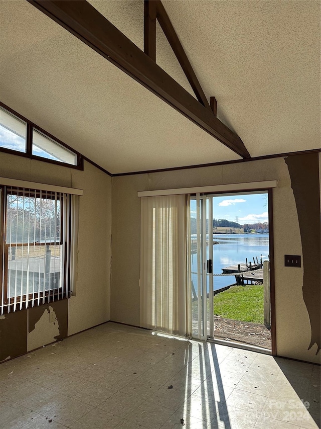 empty room featuring lofted ceiling with beams, a water view, and a textured ceiling