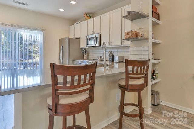 kitchen featuring stainless steel appliances, light hardwood / wood-style flooring, backsplash, a breakfast bar, and white cabinets