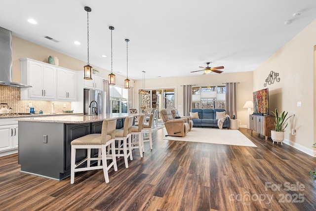 kitchen featuring backsplash, white cabinets, a center island with sink, decorative light fixtures, and dark hardwood / wood-style flooring