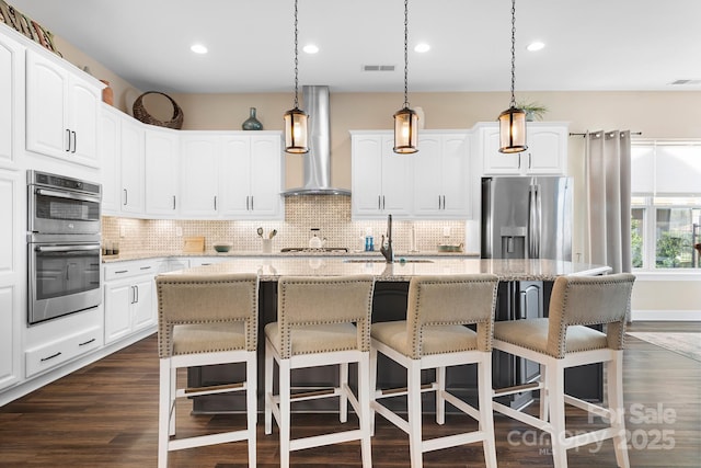 kitchen featuring a center island with sink, white cabinets, sink, wall chimney exhaust hood, and appliances with stainless steel finishes