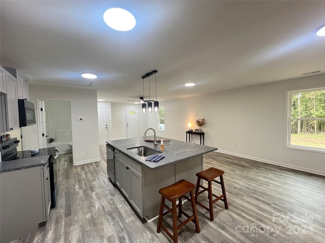 kitchen featuring pendant lighting, a center island with sink, sink, light hardwood / wood-style flooring, and range with electric stovetop