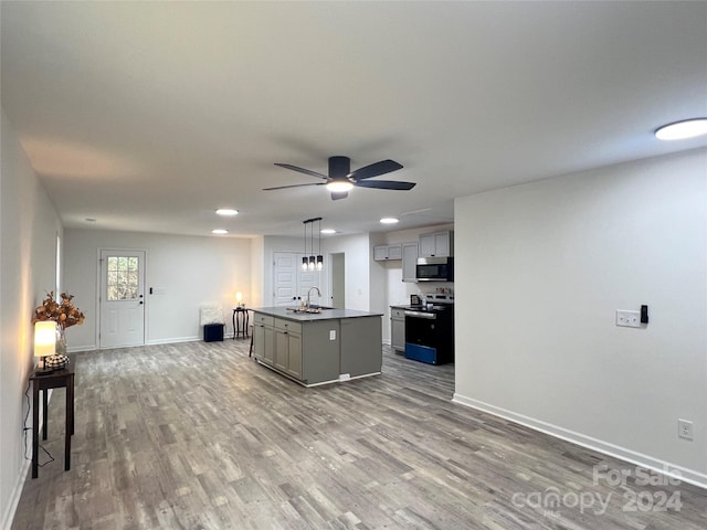 kitchen with gray cabinetry, sink, hardwood / wood-style flooring, an island with sink, and appliances with stainless steel finishes