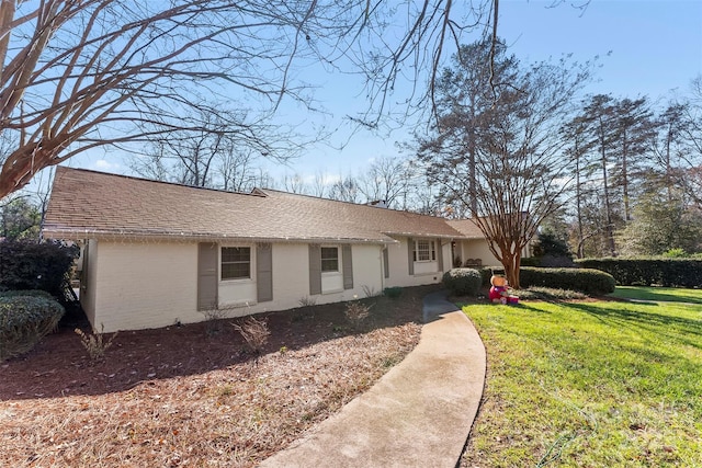 ranch-style house featuring a shingled roof, brick siding, and a front lawn