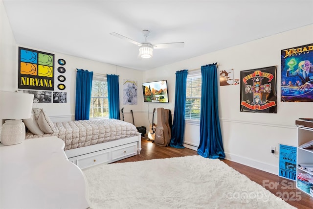 bedroom with dark wood-style floors, a baseboard heating unit, multiple windows, and ceiling fan