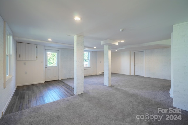 basement with dark wood-type flooring, brick wall, and a baseboard heating unit