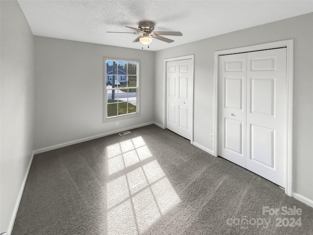 unfurnished bedroom with multiple closets, ceiling fan, dark carpet, and a textured ceiling