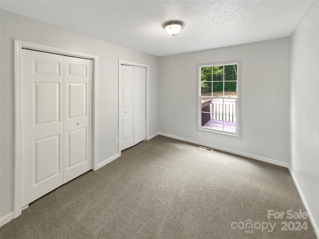 unfurnished bedroom featuring carpet flooring, a textured ceiling, and two closets