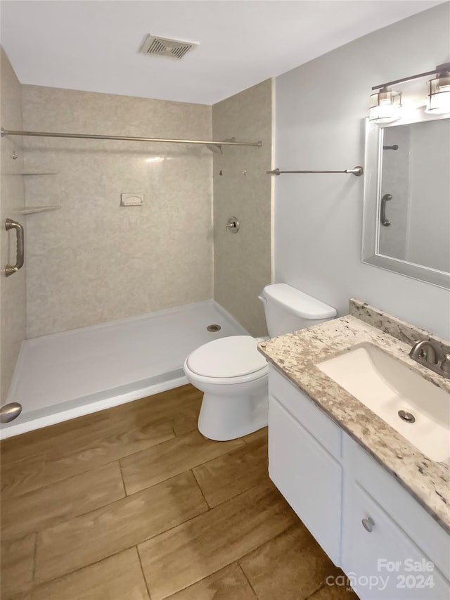 bathroom with vanity, toilet, wood-type flooring, and a tile shower