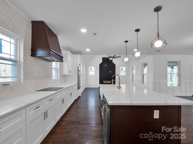 kitchen with white cabinets, custom exhaust hood, a spacious island, decorative light fixtures, and a fireplace