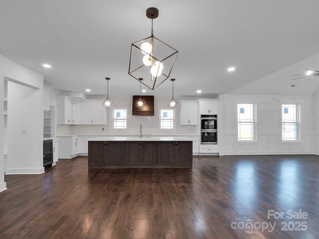 kitchen with tasteful backsplash, wine cooler, a kitchen island with sink, and white cabinetry