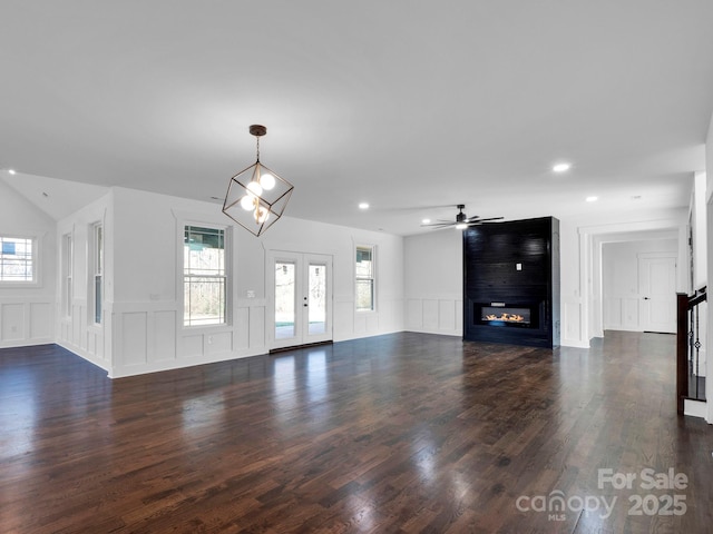 unfurnished living room featuring ceiling fan with notable chandelier, a large fireplace, dark wood-type flooring, and french doors