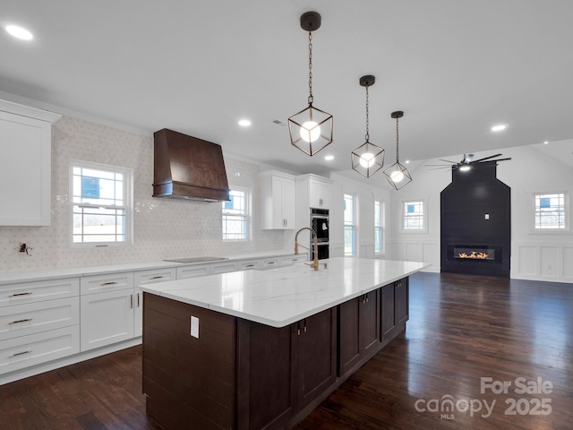 kitchen featuring premium range hood, pendant lighting, a fireplace, white cabinetry, and a large island