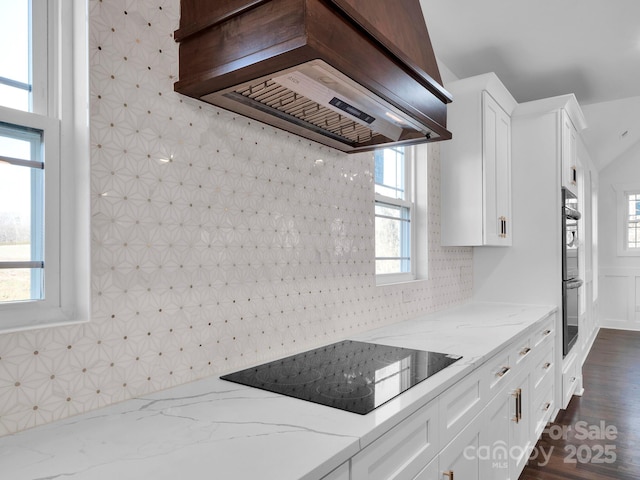 kitchen with black appliances, white cabinetry, light stone counters, and custom range hood