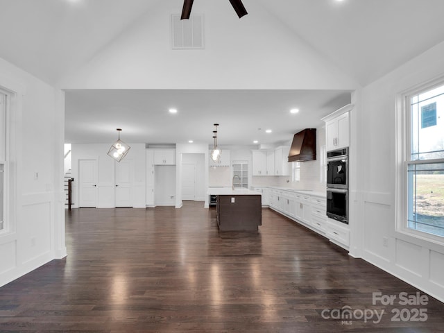 kitchen with a center island, white cabinets, double oven, decorative light fixtures, and custom range hood