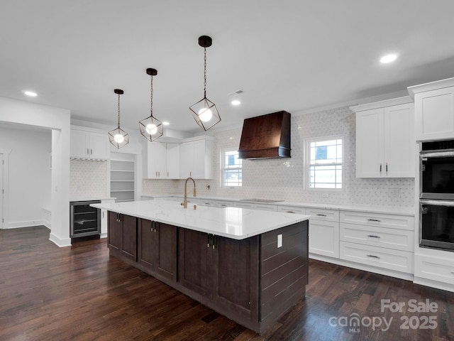 kitchen featuring white cabinets, an island with sink, wine cooler, and custom exhaust hood