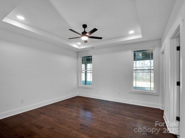 empty room with a tray ceiling, ceiling fan, and dark wood-type flooring