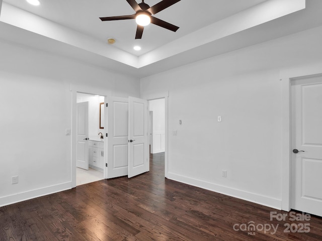 unfurnished bedroom featuring dark hardwood / wood-style flooring, ensuite bathroom, a raised ceiling, and ceiling fan