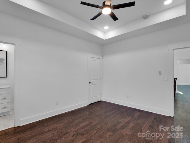 unfurnished room with ceiling fan, a raised ceiling, and dark wood-type flooring