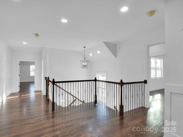 hallway featuring a healthy amount of sunlight, dark hardwood / wood-style flooring, vaulted ceiling, and an inviting chandelier