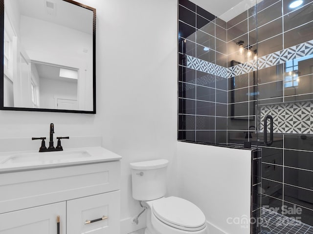 bathroom featuring a tile shower, vanity, and toilet