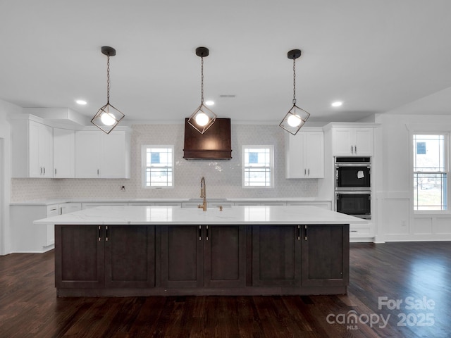 kitchen with plenty of natural light, white cabinetry, a kitchen island with sink, and double oven