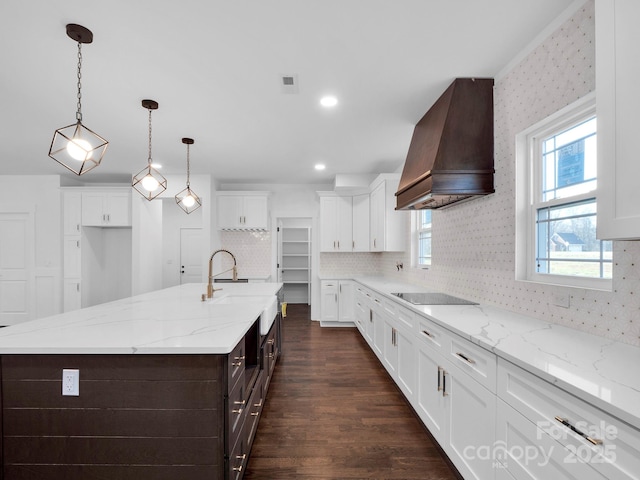 kitchen with light stone counters, custom range hood, a spacious island, white cabinetry, and hanging light fixtures