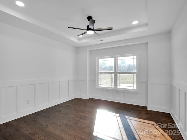 empty room with a raised ceiling, ceiling fan, and dark hardwood / wood-style floors