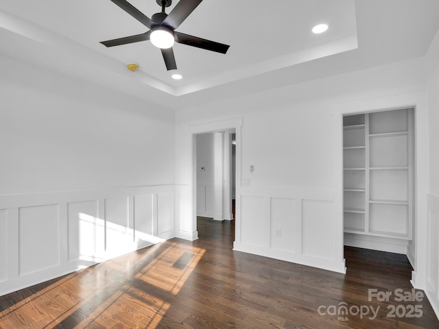 interior space with a closet, ceiling fan, a tray ceiling, and dark hardwood / wood-style floors