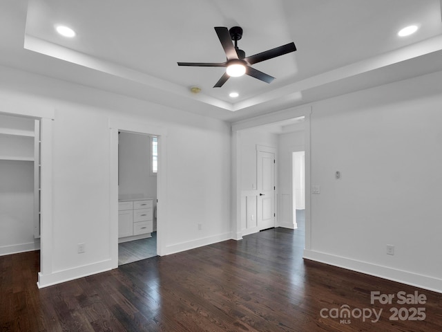 unfurnished bedroom featuring dark wood-type flooring, a walk in closet, ceiling fan, connected bathroom, and a tray ceiling