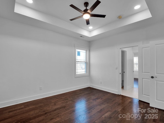 unfurnished room with dark hardwood / wood-style floors, a healthy amount of sunlight, ceiling fan, and a tray ceiling