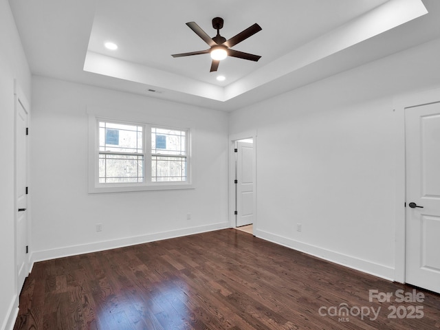 empty room with a raised ceiling, ceiling fan, and dark hardwood / wood-style floors