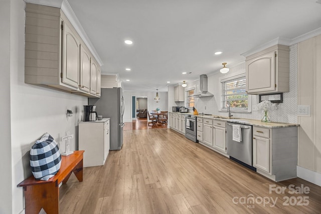 kitchen featuring appliances with stainless steel finishes, sink, wall chimney exhaust hood, crown molding, and light hardwood / wood-style flooring