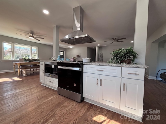 kitchen featuring wall chimney range hood, hardwood / wood-style flooring, light stone counters, white cabinetry, and stainless steel appliances