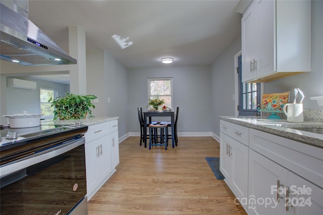 kitchen featuring light stone countertops, light hardwood / wood-style flooring, white cabinets, and wall chimney range hood